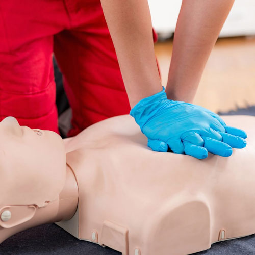 Person performing chest compressions on a CPR training manikin wearing blue gloves