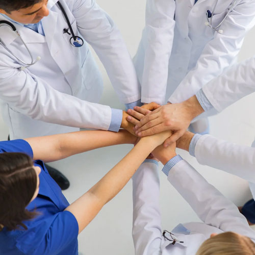 A diverse group of healthcare professionals joins hands, symbolizing teamwork and collaboration in a supportive medical setting.