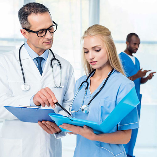 Two healthcare professionals in white lab coats and scrubs discuss patient information, while another colleague stands in the background.