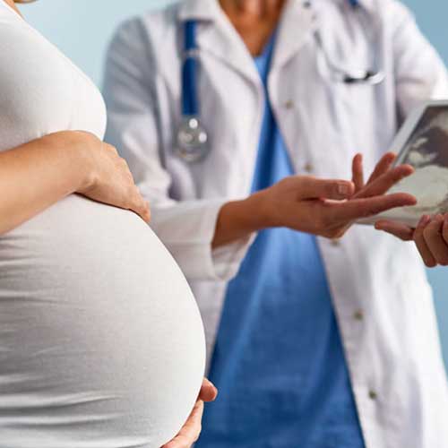 A pregnant woman in a white dress is speaking with a healthcare professional in a lab coat, discussing an ultrasound image.
