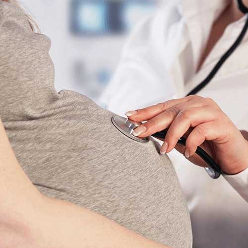 A healthcare professional uses a stethoscope to listen to the heartbeat of a pregnant woman's abdomen.