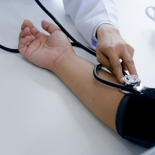 A healthcare professional measures a patient's blood pressure using a stethoscope and sphygmomanometer on their arm.