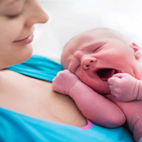A close-up of a mother holding her newborn baby against her chest, both cuddled in a moment of tenderness and connection.