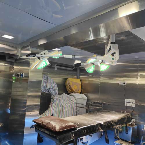 Two medical professionals in blue scrubs and masks perform surgery, focused on a patient under bright surgical lights.